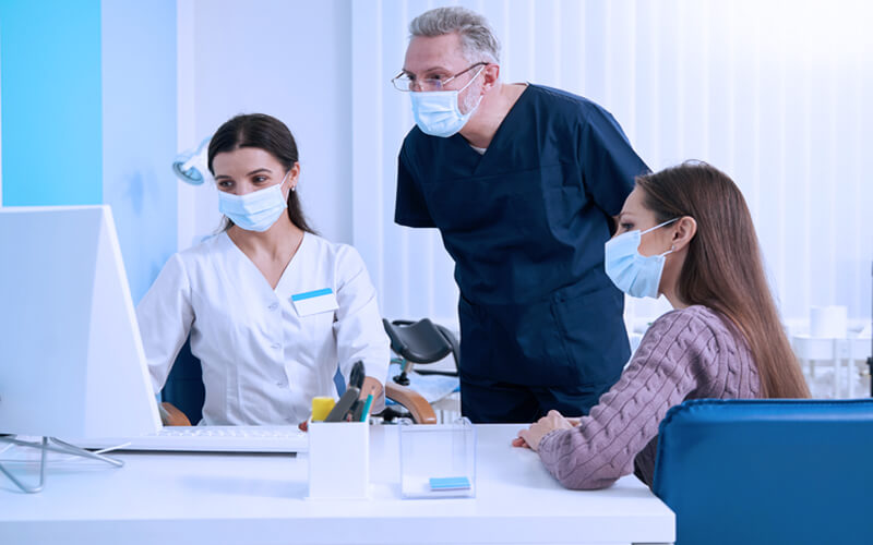 Paciente sendo atendida por dois médicos, com todos usando máscara, em consultório médico