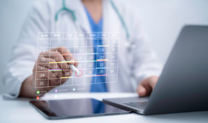 Médica ao fundo preenchendo uma agenda online holográfica sobre um tablet