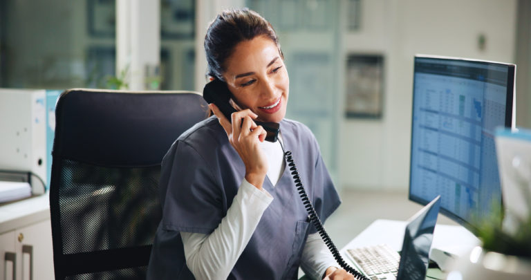 Recepcionista de clínica médica em seu ambiente de trabalho falando ao telefone