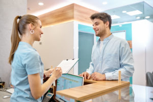 Recepcionista de clínica médica atendendo um paciente segurando uma prancheta