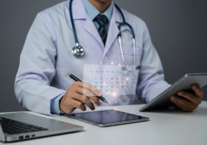 Agendamento de consulta online: benefícios para médicos e pacientes 1 Médico de jaleco branco e estetoscópio usando dois tablets e um notebook para otimizar agenda