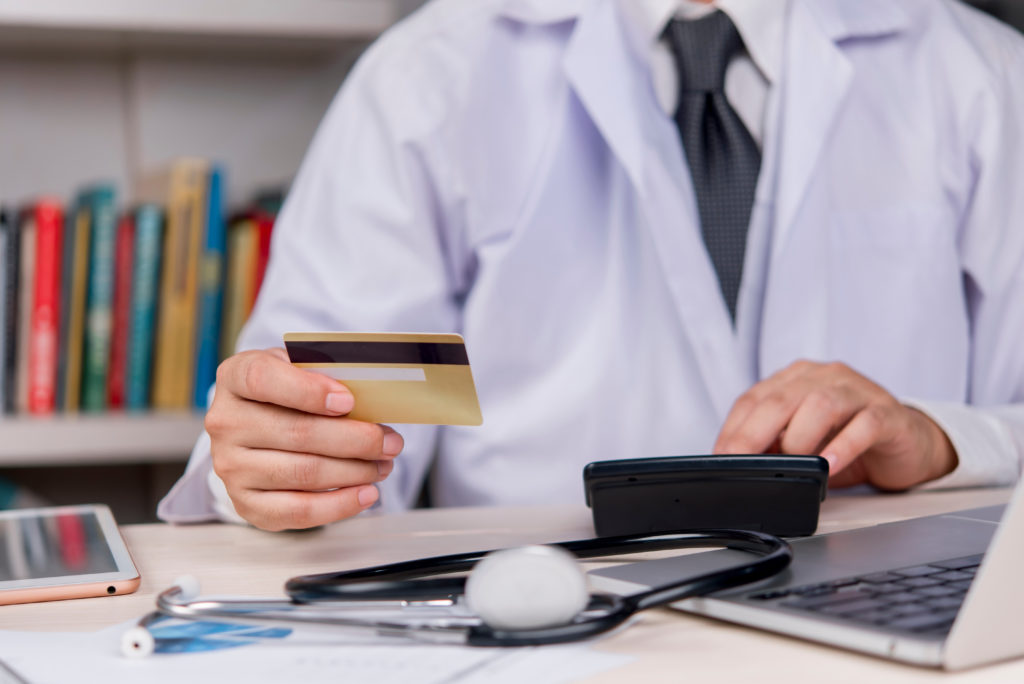 Médico em um consultório segurando um cartão de crédito