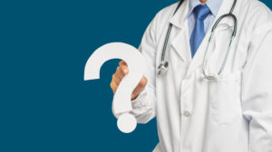 Tire suas dúvidas e escolha o software de gestão para consultórios ideal 1 Médico de jaleco branco segurando um ponto de interrogação grande e branco