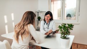 Médica atendendo uma paciente em consulta mostrando dados em um tablet