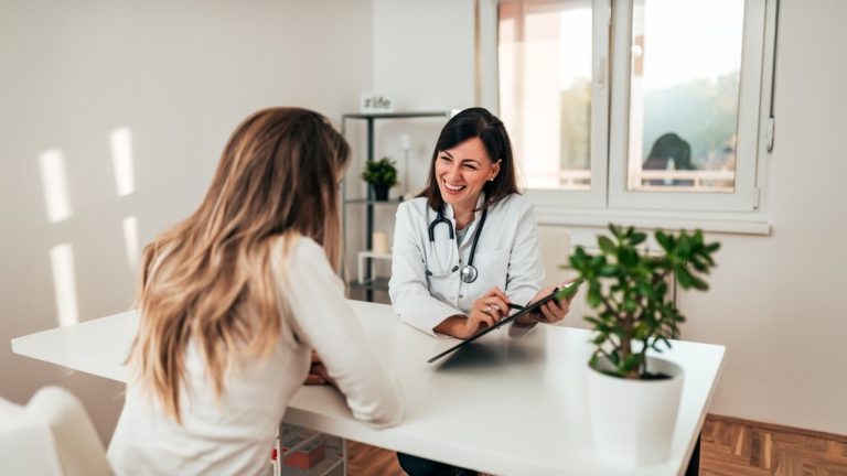Médica atendendo uma paciente em consulta mostrando dados em um tablet