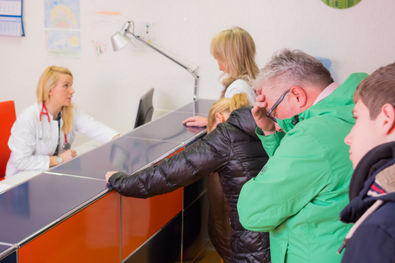 Recepção de clínica cheia de pacientes em fila com recepcionista sobrecarregada