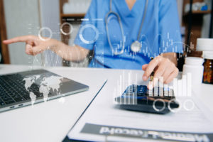 Médico usando calculadora e laptop para analisar custos de saúde, simbolizando o impacto da rentabilidade na gestão financeira médica