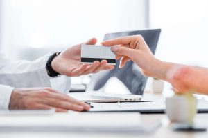 Dicas para negociar melhores taxas com operadoras de cartão e planos de saúde 1 Paciente entregando cartão de crédito a médico em clínica, simbolizando relação financeira na saúde